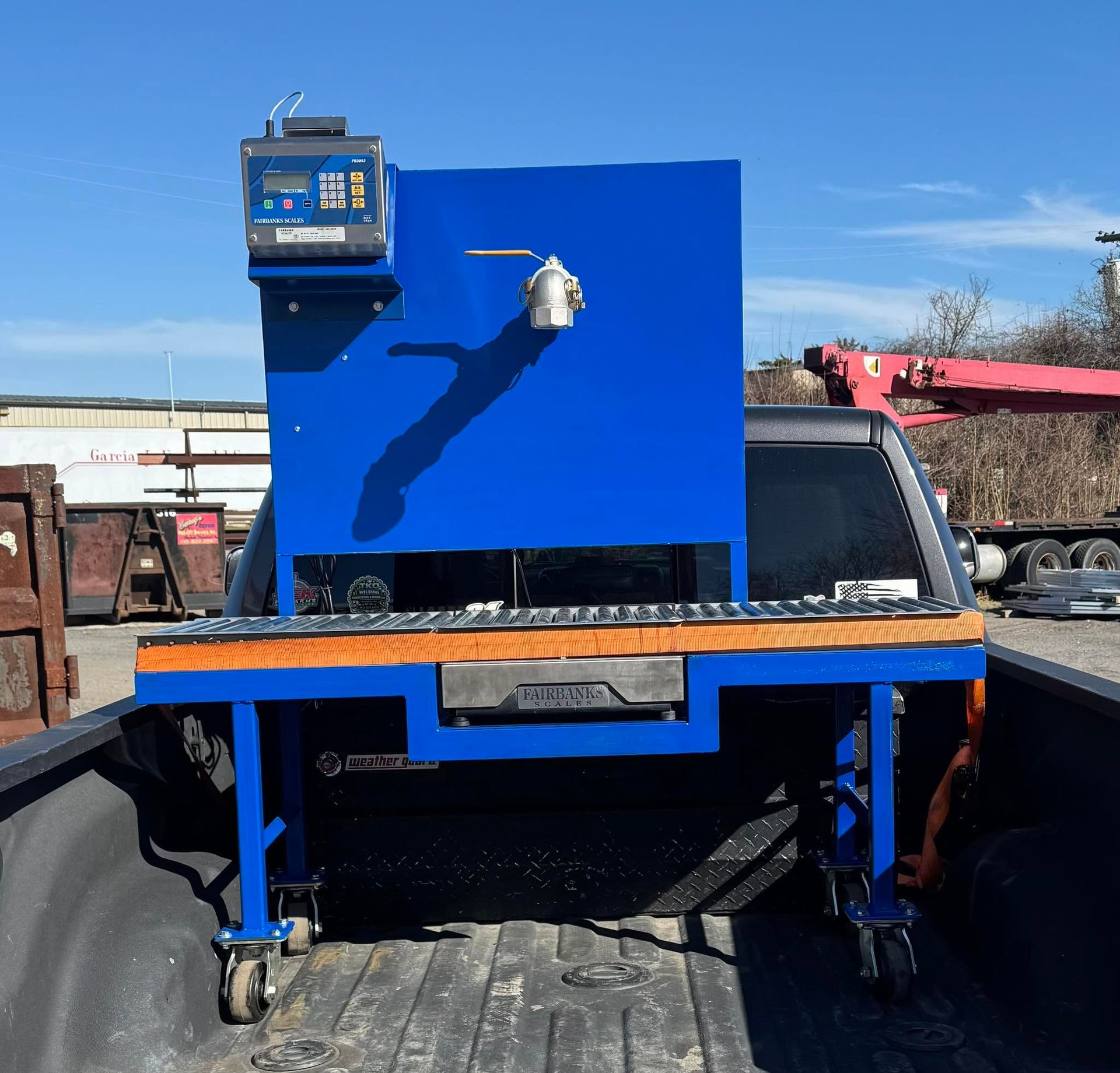 Blue industrial hopper with control panel mounted on a truck bed in a yard under a clear sky.