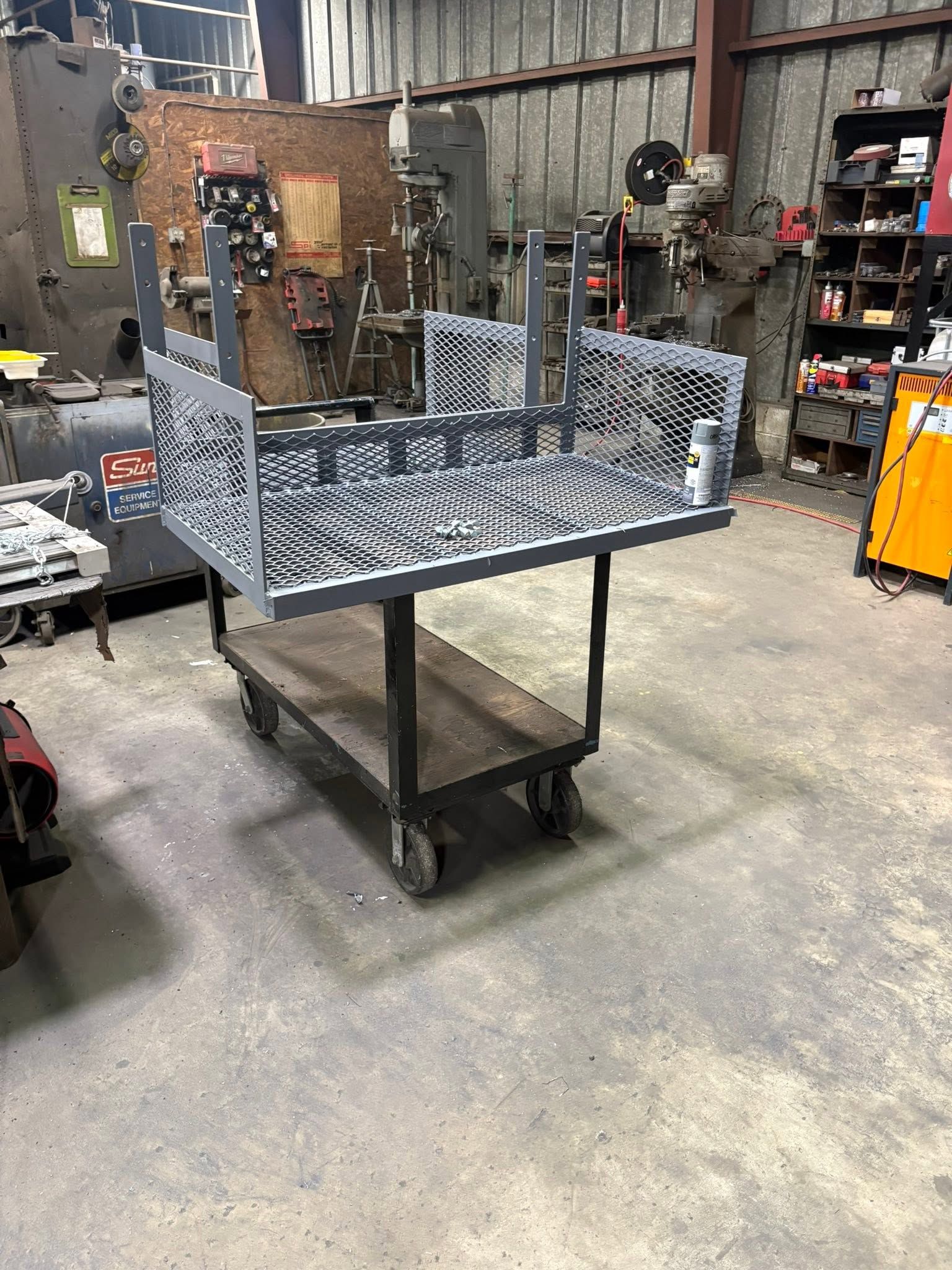 Industrial worktable with a metal fixture on casters in a workshop, surrounded by tools and equipment.