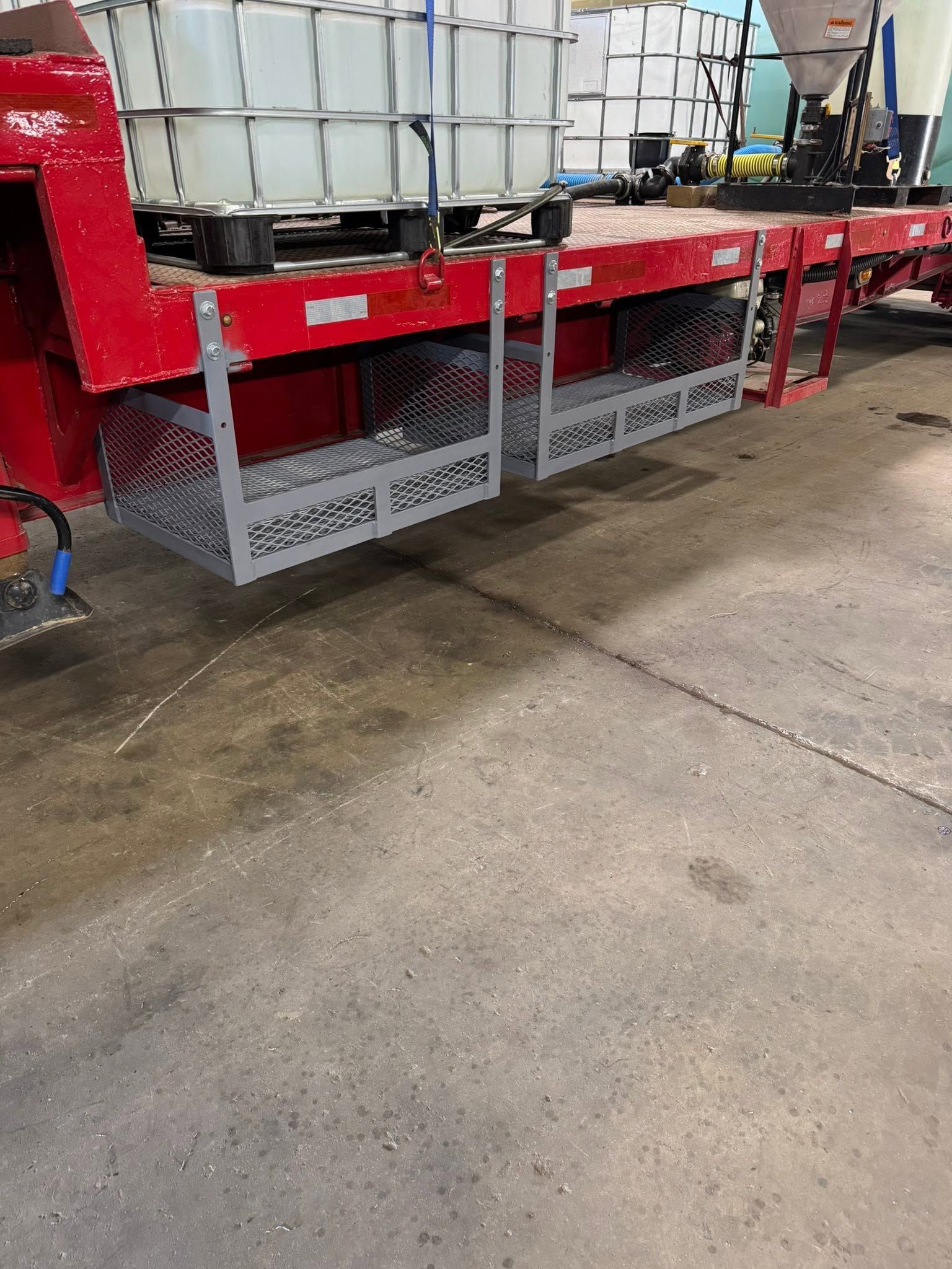 Red warehouse trailer loaded with white bulk tanks, parked on a wet concrete floor.
