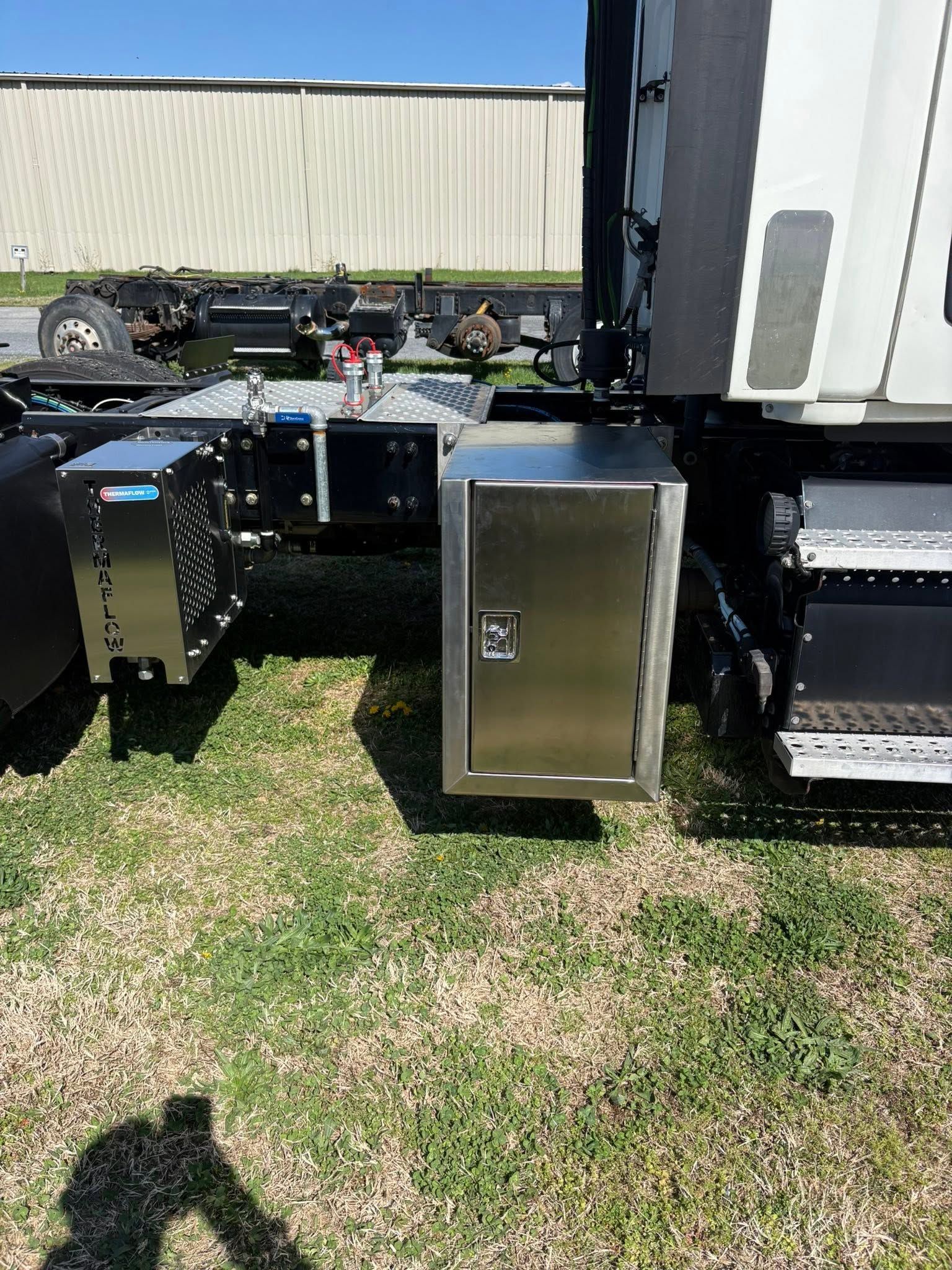 Stainless steel outdoor cabinets beside a truck trailer on grass under bright sunlight.