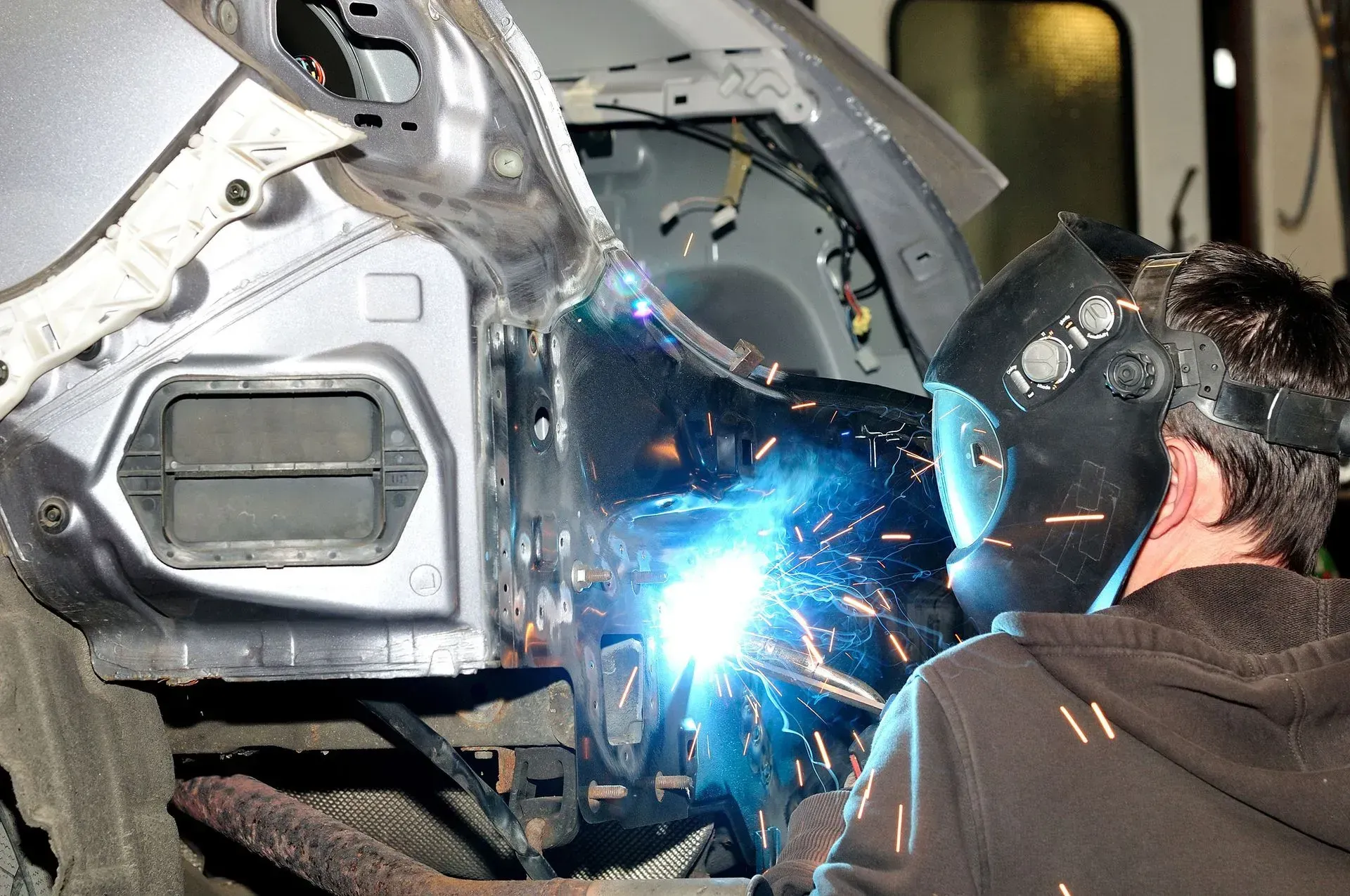 Person welding a car frame, bright blue sparks flying in a garage workshop.