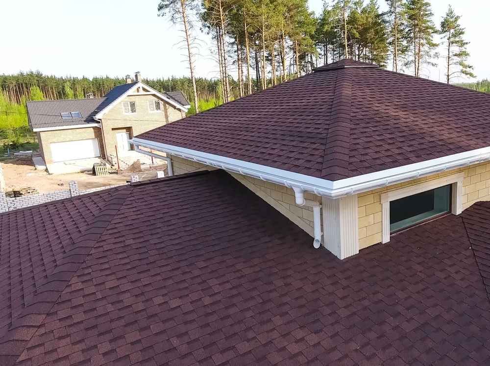 Aerial view of a red shingle roof with a dormer and neighboring house near trees