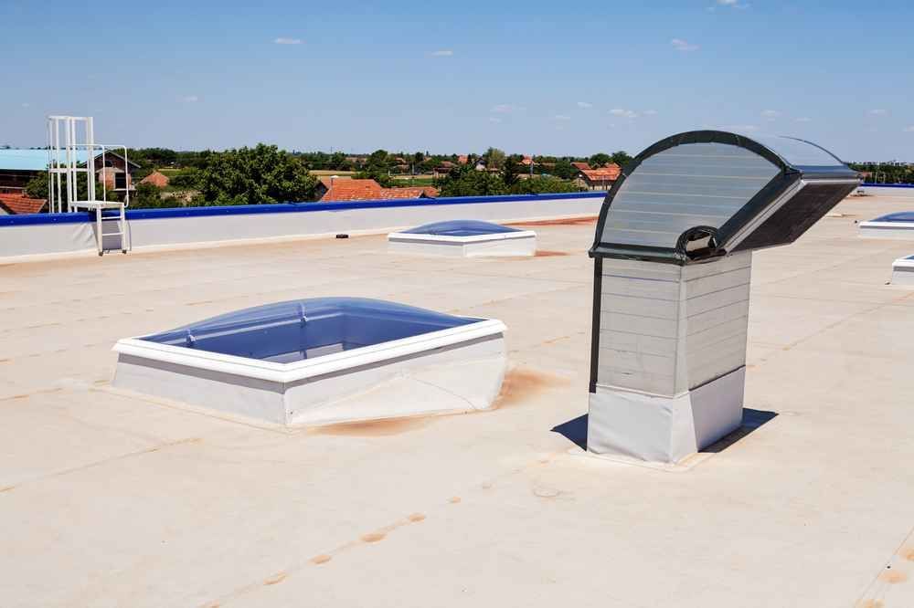 Rooftop with two skylights and a curved ventilation unit under a clear blue sky