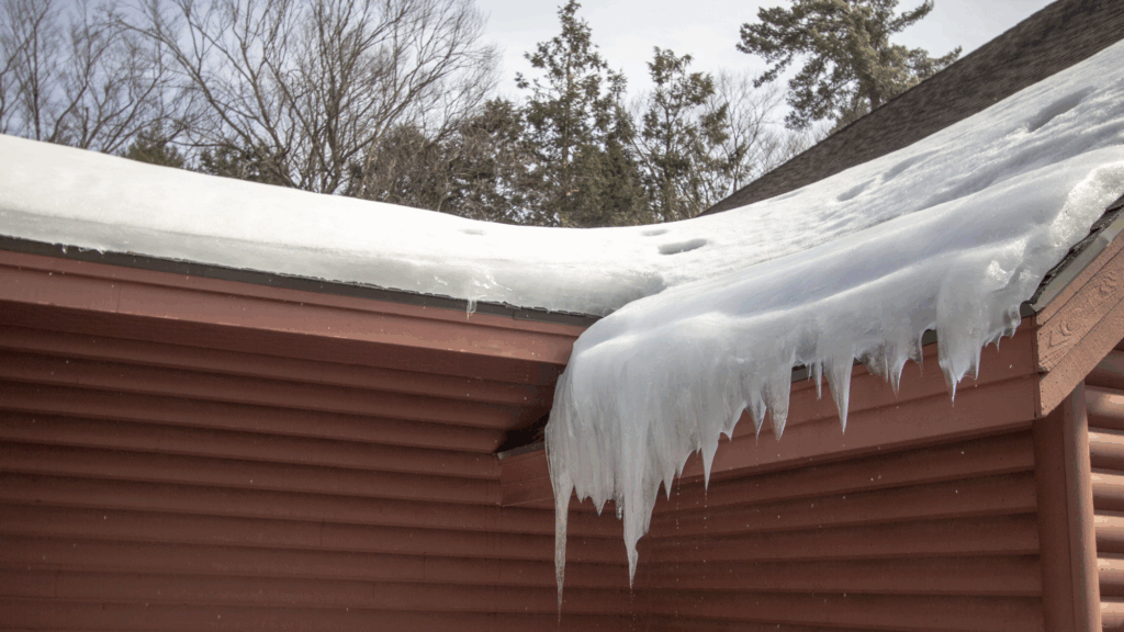 Snow-covered roof with large icicles hanging over a brown house exterior