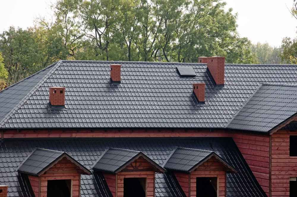 Red tiled roof with several chimneys and skylights above a brick building and trees