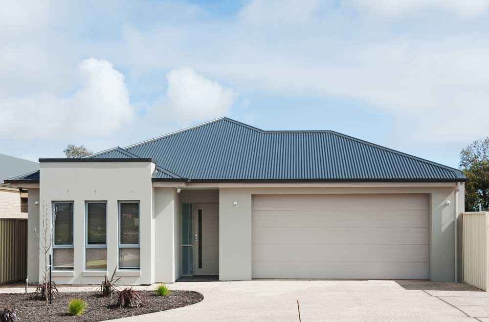 Modern single-story house with a blue roof, light exterior, and two-car garage under a cloudy sky