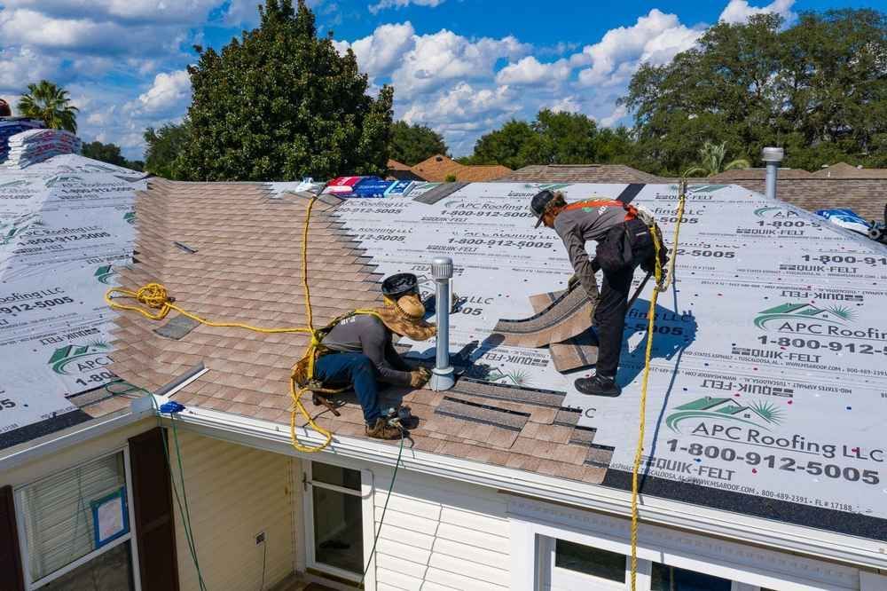 Workers replacing shingles on a white house roof under a blue sky