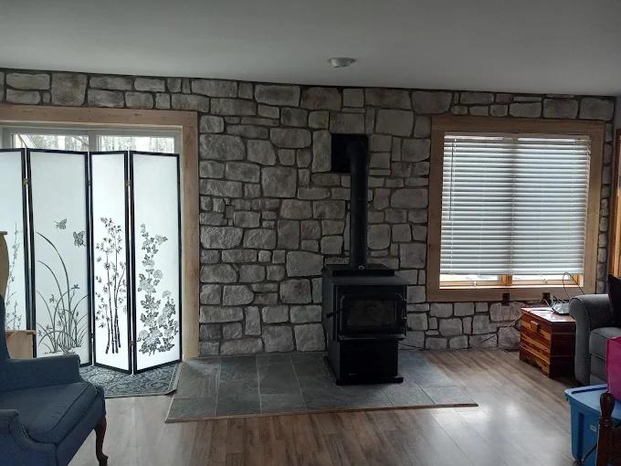 Living room with stone fireplace, wood stove, sliding glass doors, and window blinds