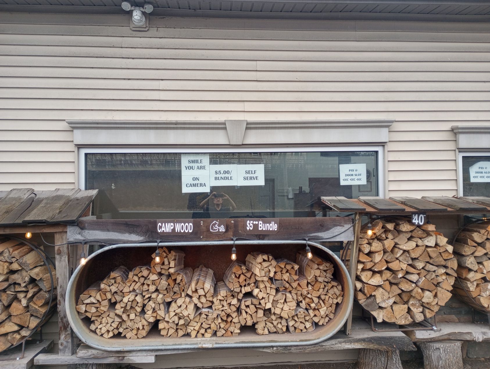 Firewood stacked in racks outside a beige building with a window display.