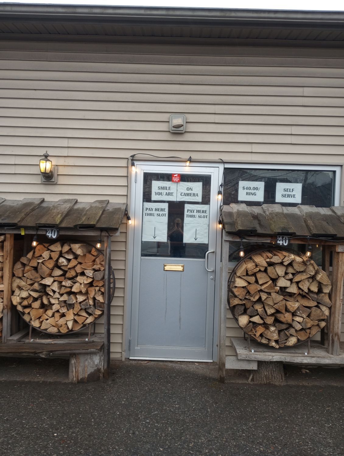 Small storefront entrance with stacked firewood on both sides and signs on the door and windows.