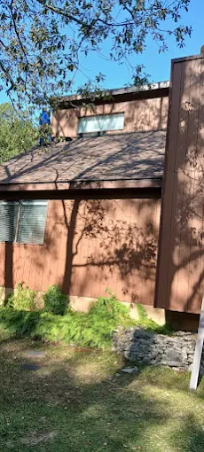 Brown house exterior with sloped roof, windows, and tree shadows on the wall