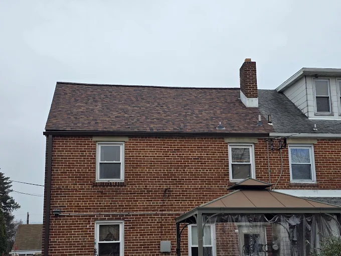 Brick house exterior with dark shingled roof and enclosed porch under an overcast sky
