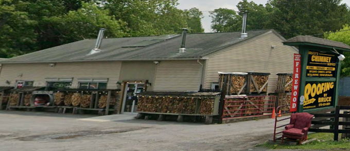 Rustic roadside store exterior with wood siding, green roof, and a large produce sign