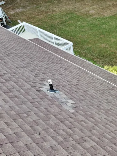Roof with a small vent pipe and a fenced grassy yard in the background.