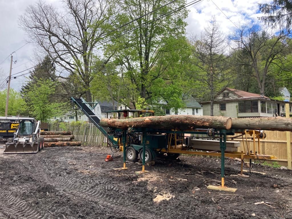 Logging truck loaded with large logs at a muddy worksite, with a bulldozer and trees in the background