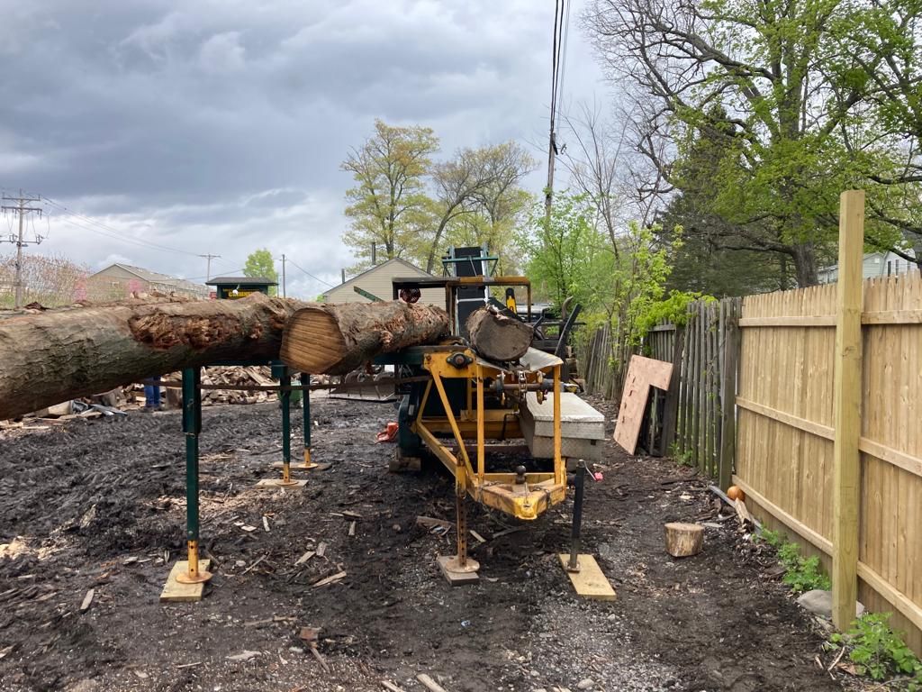 Log splitter processing a large tree trunk in a muddy backyard beside a wooden fence
