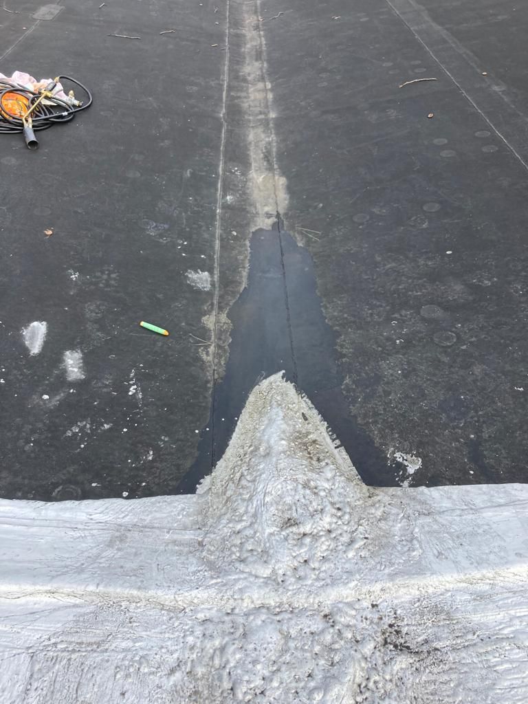 Rooftop with a raised seam and white patch against dark asphalt, with debris in the upper left.