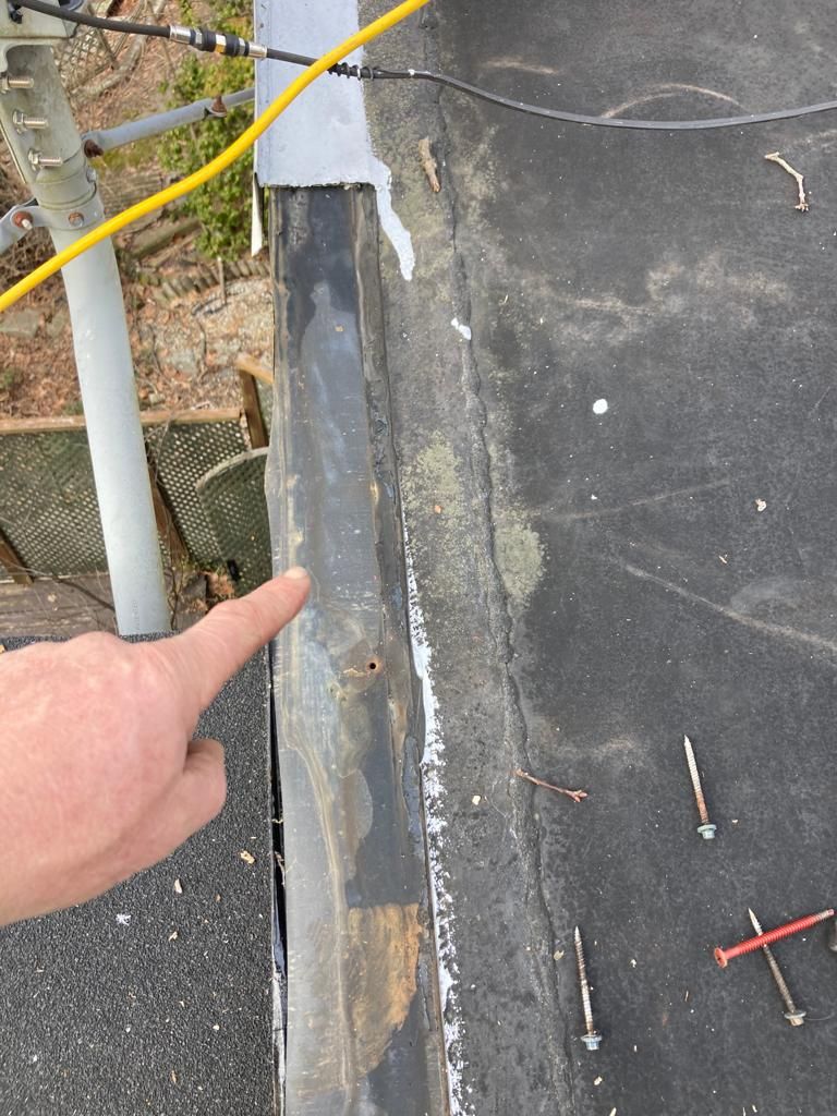Finger pointing at a damaged black waterproof membrane seam on a rooftop or wall edge