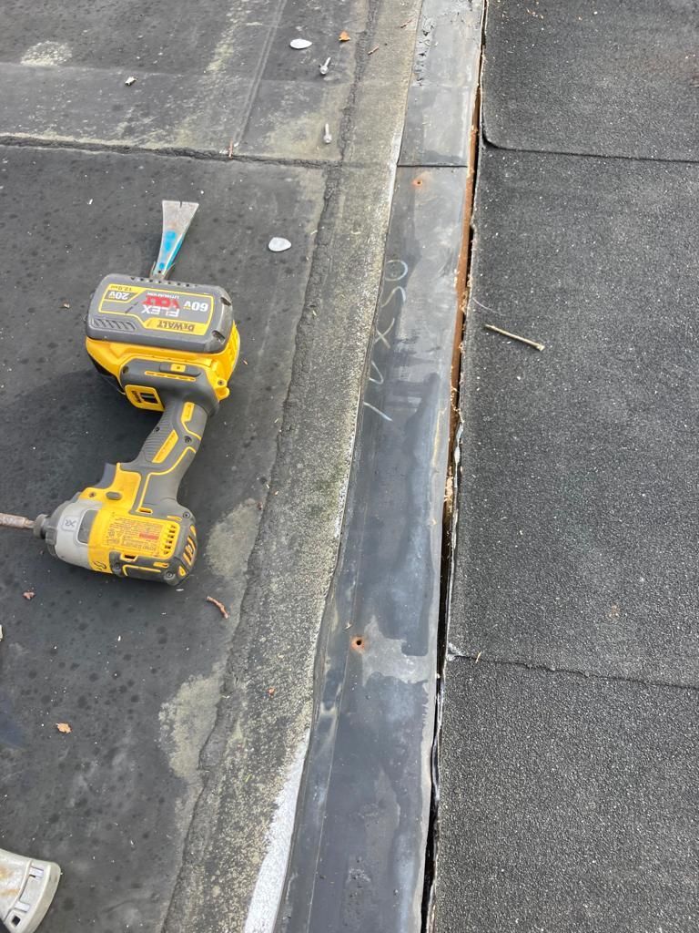 Yellow cordless drill and battery on a concrete sidewalk beside a curb and drainage channel
