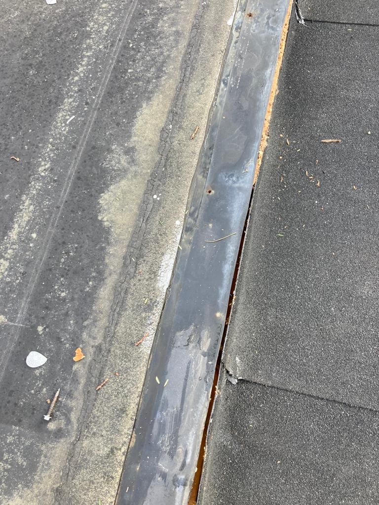 Close-up of a damaged roof seam with peeling coating and exposed rust along the edge