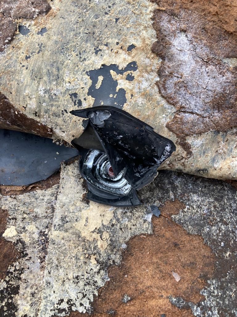 Broken black camera lens embedded in rock, with cracked glass and debris around it