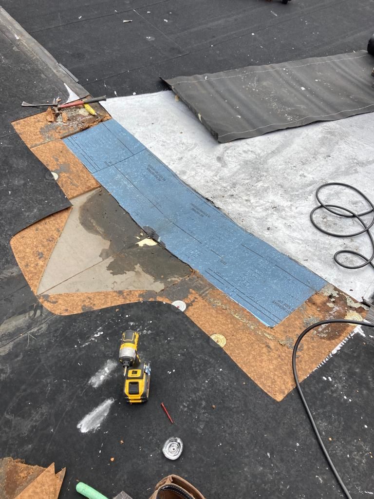 Roof repair materials and tools spread across a flat roof, including blue and orange underlayment strips.