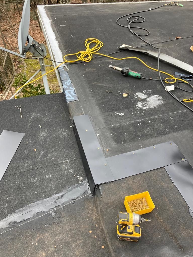 Roof repair with black roofing felt, gray flashing, tools, and a yellow cordless drill on a flat roof.