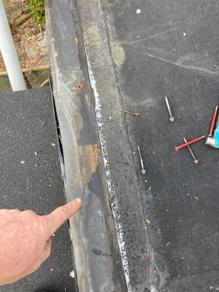 Finger pointing at a cracked seam between two pavement surfaces next to gravel and tools