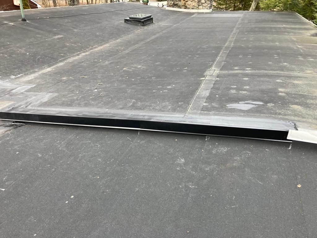 Loose black roofing membrane lifting on a flat roof, creating a visible gap at the seam.