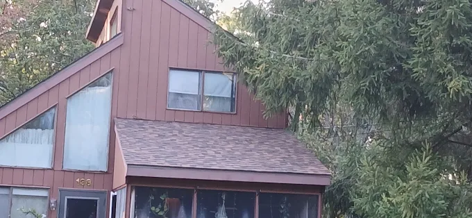 Wooden house with large windows and a steep roof, partly hidden by trees.