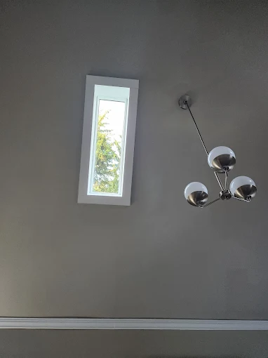 Ceiling view with a narrow skylight and a modern three-bulb chandelier against a gray ceiling.