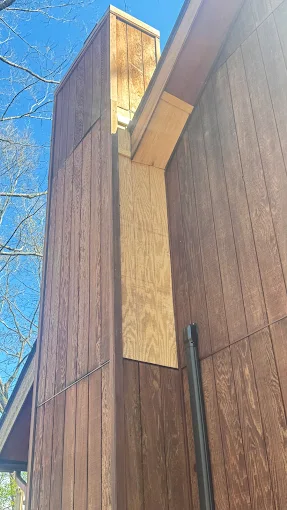 Tall wooden building corner with a narrow light-colored panel between brown walls and blue sky above