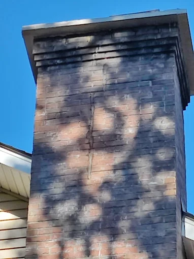 Brick chimney with a painted face mural against a blue sky