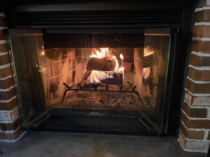 Lit fireplace with bright flames behind a black metal screen, framed by brick.