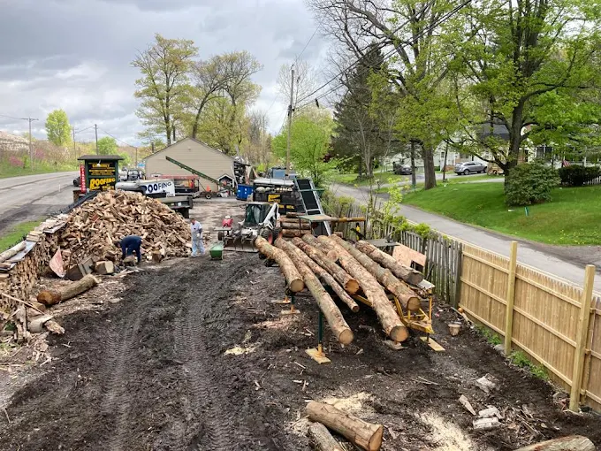Mud-covered construction site with stacked logs, dirt piles, a parked truck, and a wooden fence along a road.