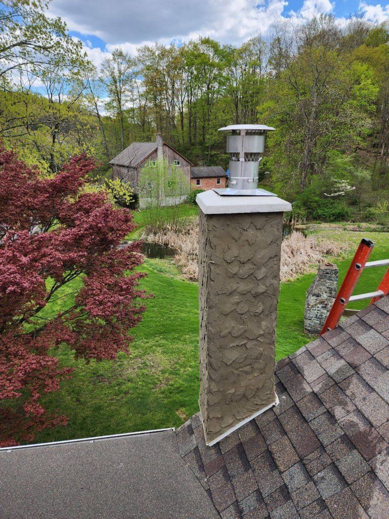Rooftop view of a stone chimney, red shingles, and a leafy backyard with a shed and trees