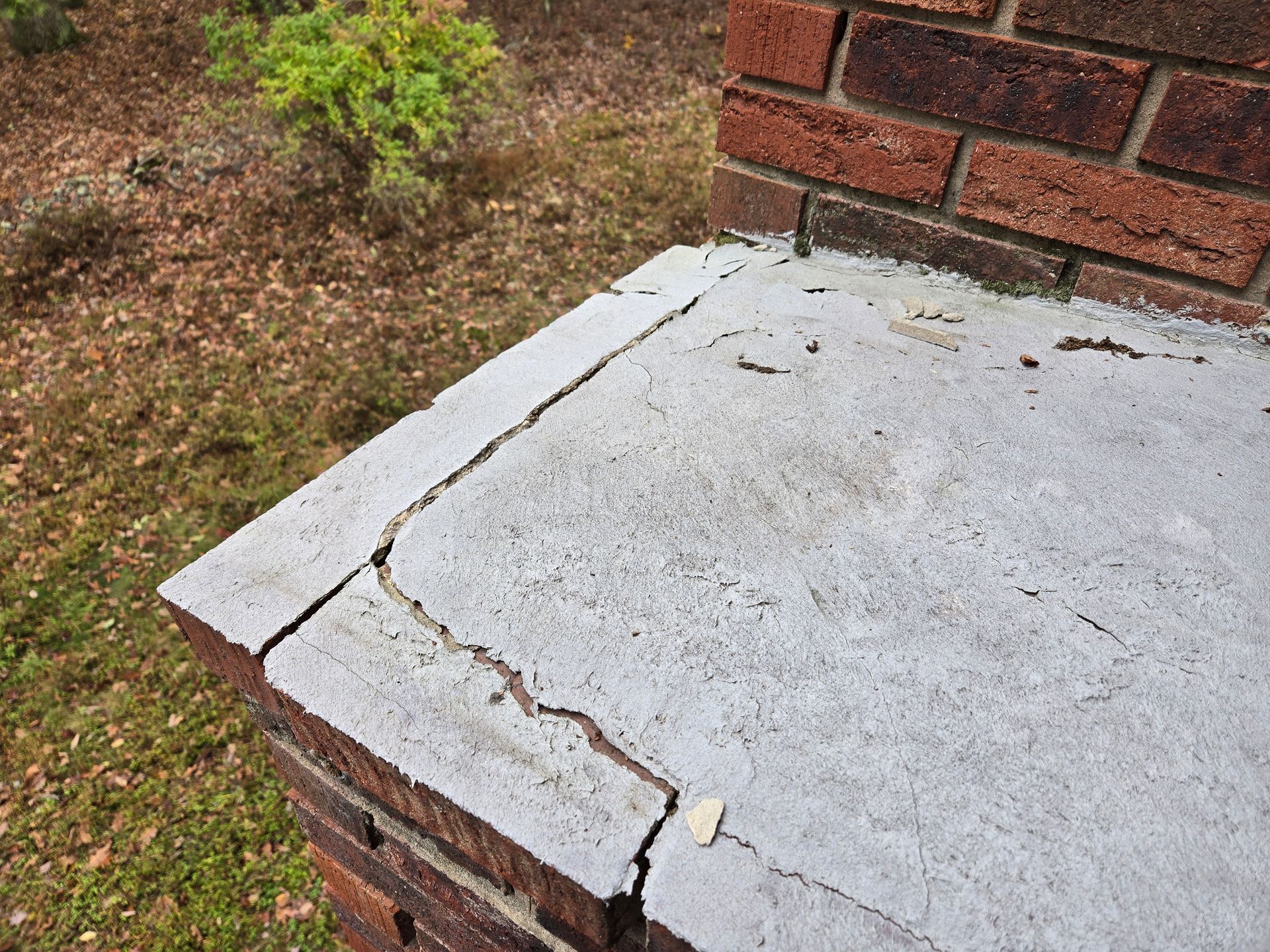Cracked white concrete cap on a brick corner wall beside a grassy yard.