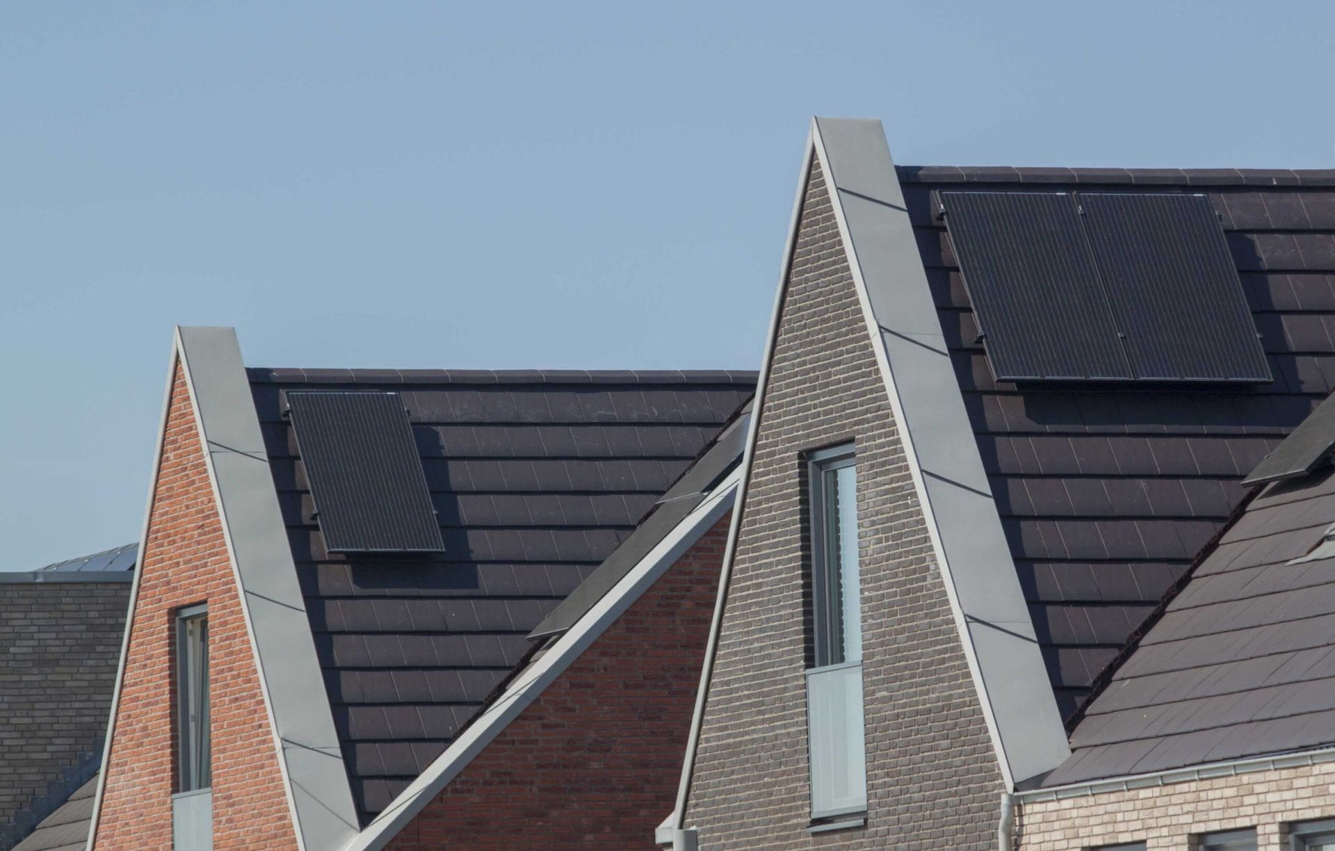 Modern house rooftops with dark solar panels and triangular brick gables under a blue sky