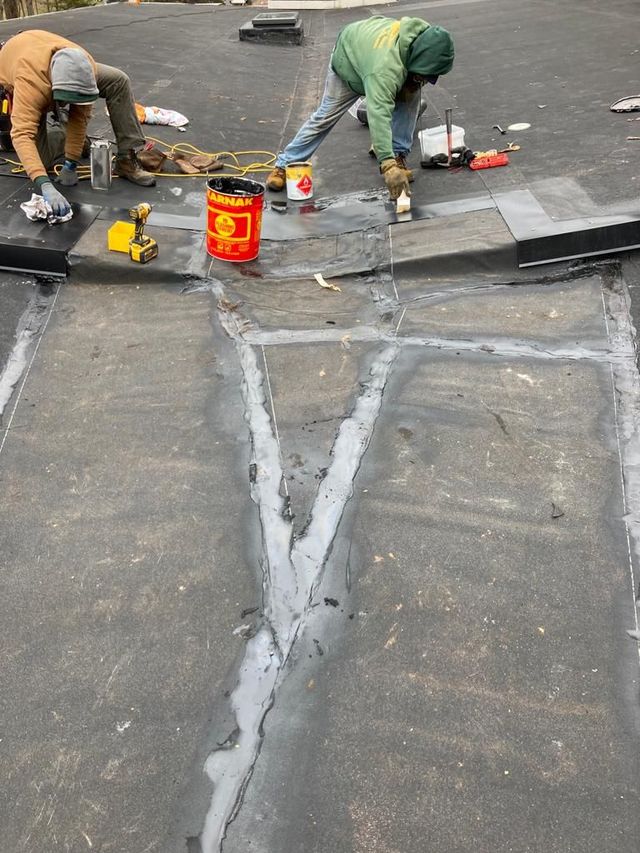 Workers repairing a flat rooftop seam with sealant and tools on a weathered roof.