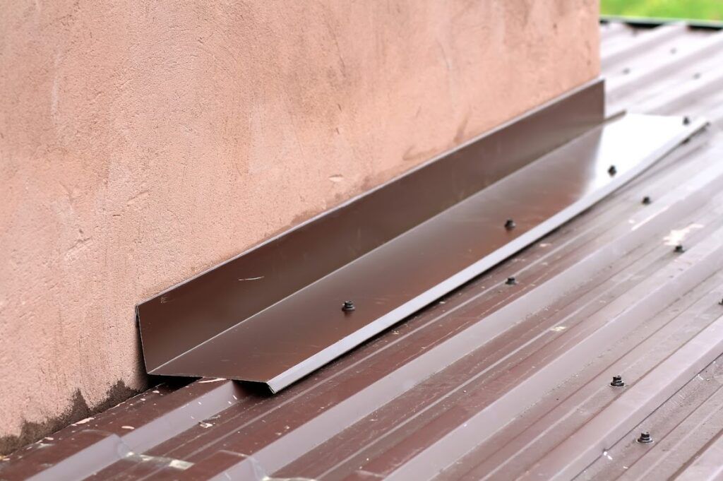 Metal roof flashing installed along the base of a stucco wall above corrugated roofing panels