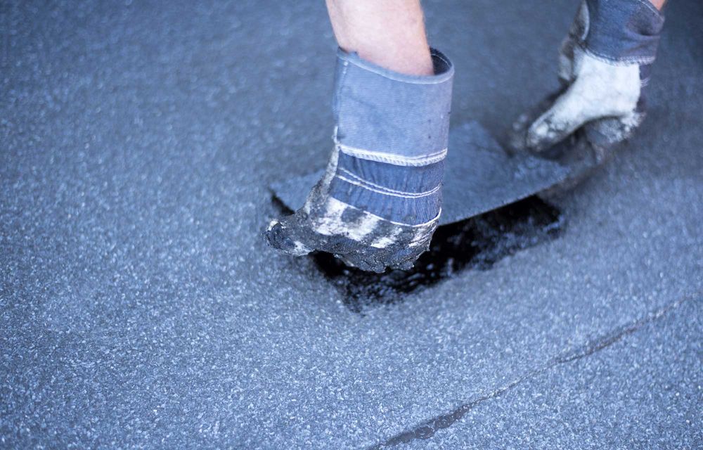 Boot stepping into wet asphalt, leaving a torn patch in the road