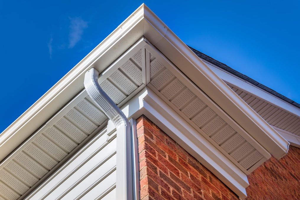 Close-up of house eaves with white soffit, gutter, and red brick wall against a blue sky