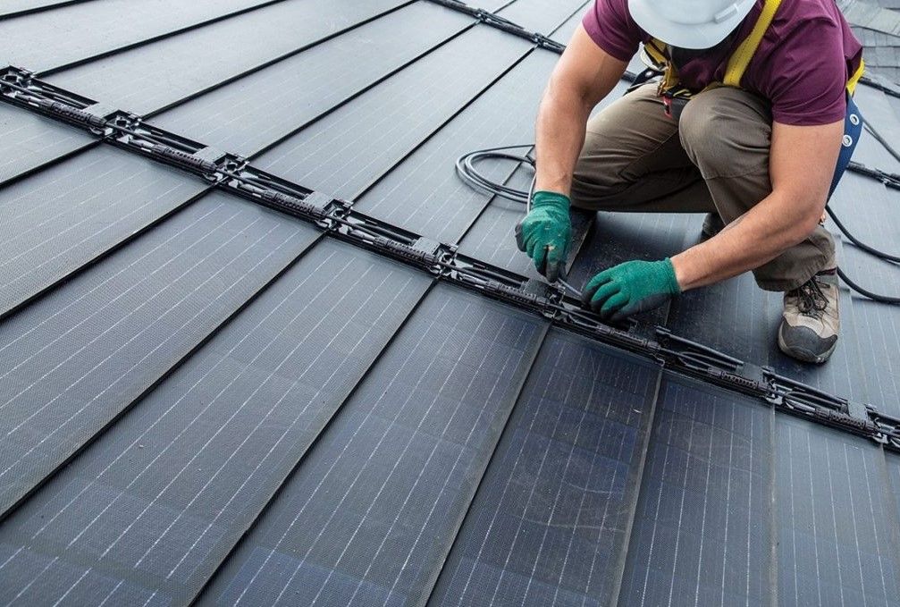 Worker installing black solar panels on a sloped roof