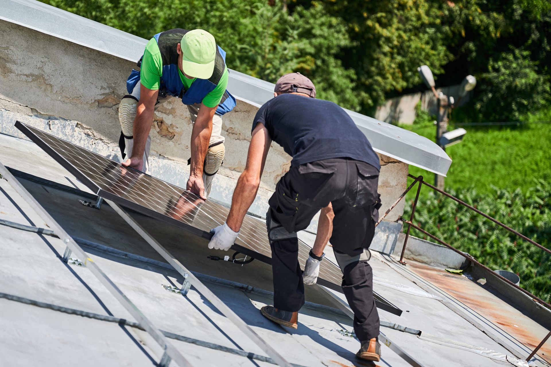 Two workers installing roof panels on a sloped rooftop, wearing safety gear and gloves.