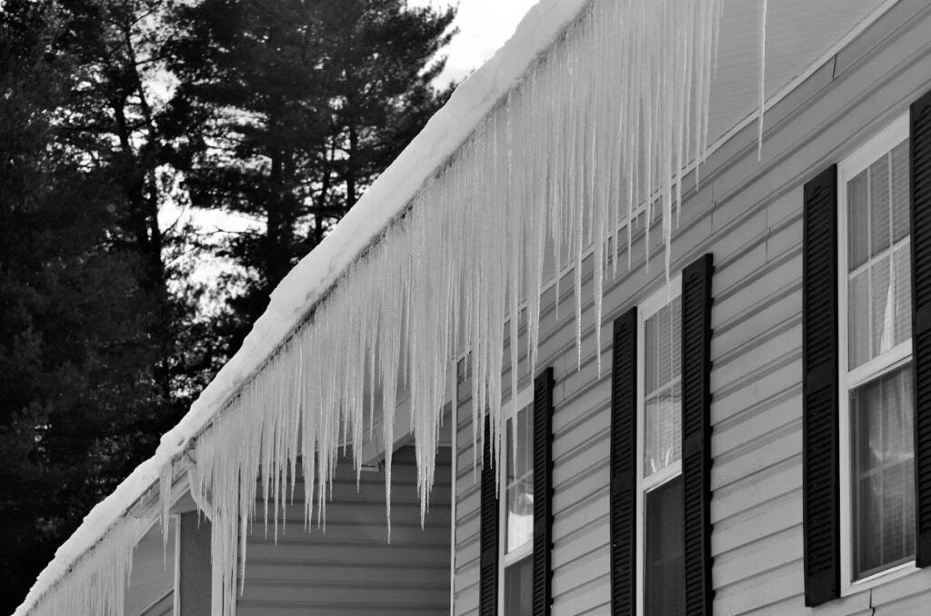 Icicles hanging from a house roof beside windows on a snowy winter day