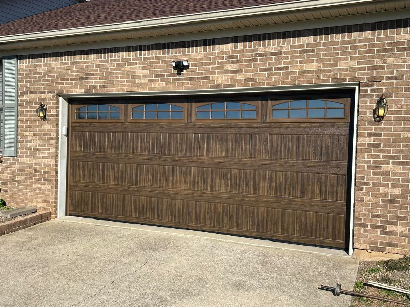 A brown garage door is sitting in front of a brick house.