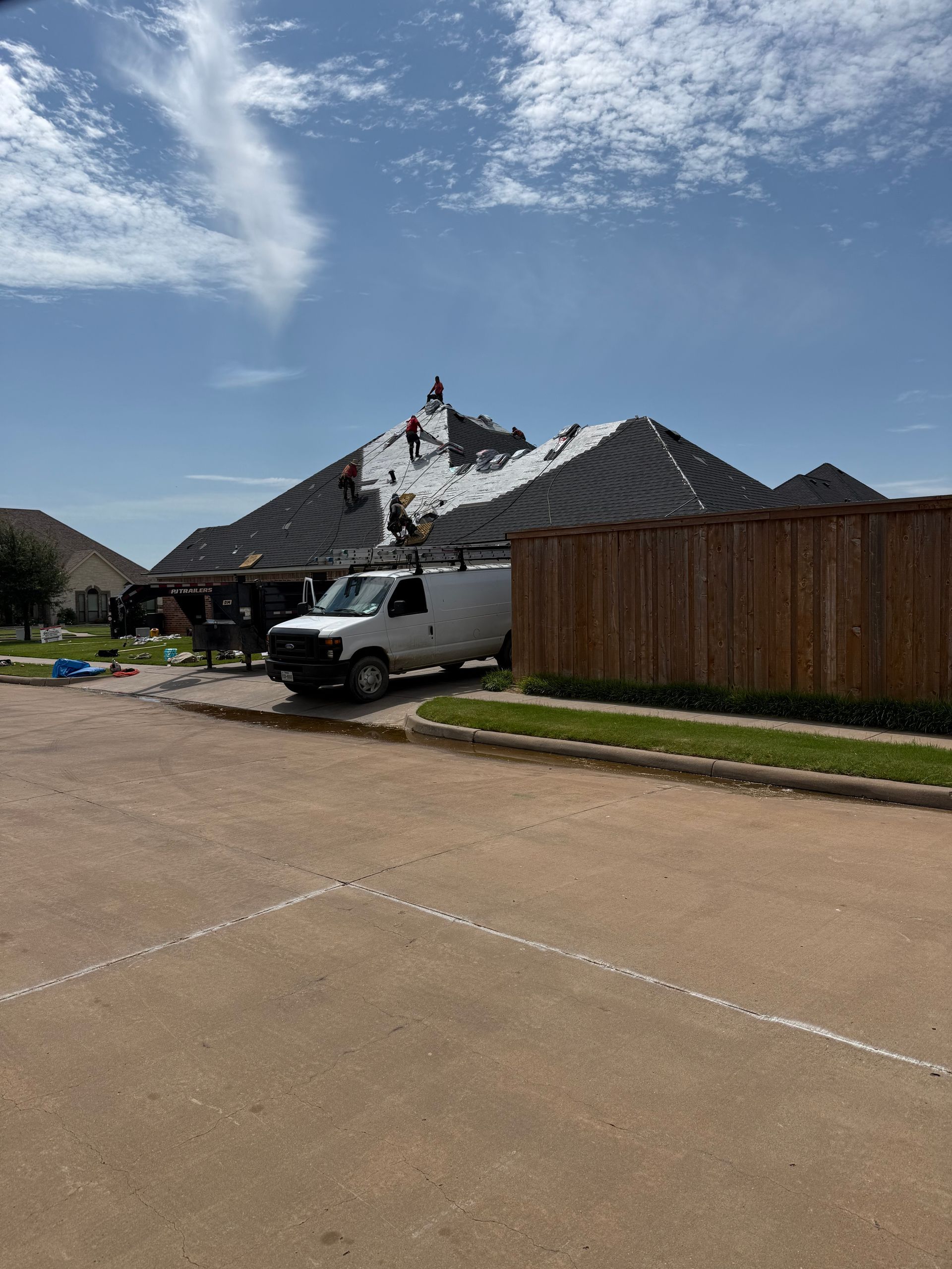 A white van parked near a house with roofing work in progress under a blue sky.