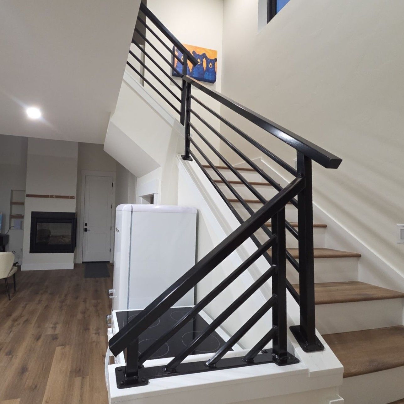 Modern black metal railings with diagonal bars installed on stairs with light wood treads in a contemporary living space.