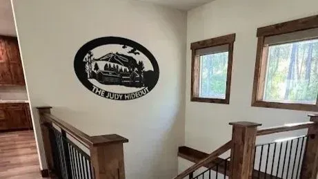 A staircase with wooden railings and metal balusters features a round, black metal wall sign reading 