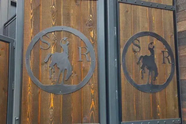 Two wooden doors with dark metal frames, each featuring a cutout logo of a bucking horse between the letters S and R.